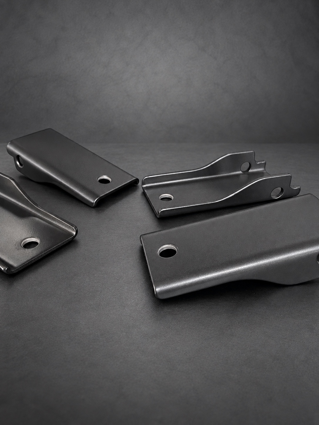 Black Cerakote E Series folded brackets arranged on a textured grey surface