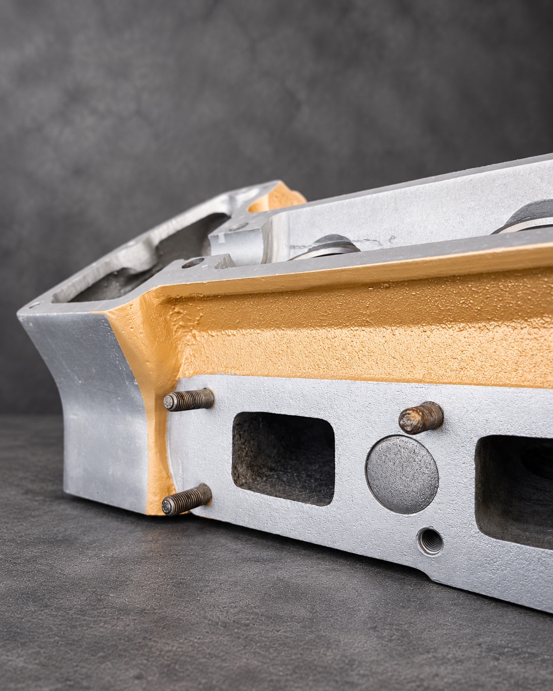 Side detail of a gold Cerakote H Series cylinder head with exposed alloy ports and studs