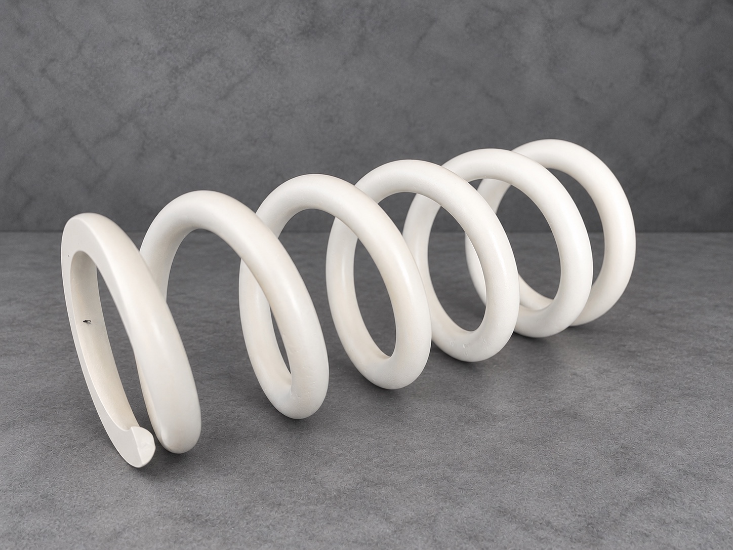 White Cerakote H Series suspension spring resting horizontally on a textured grey surface