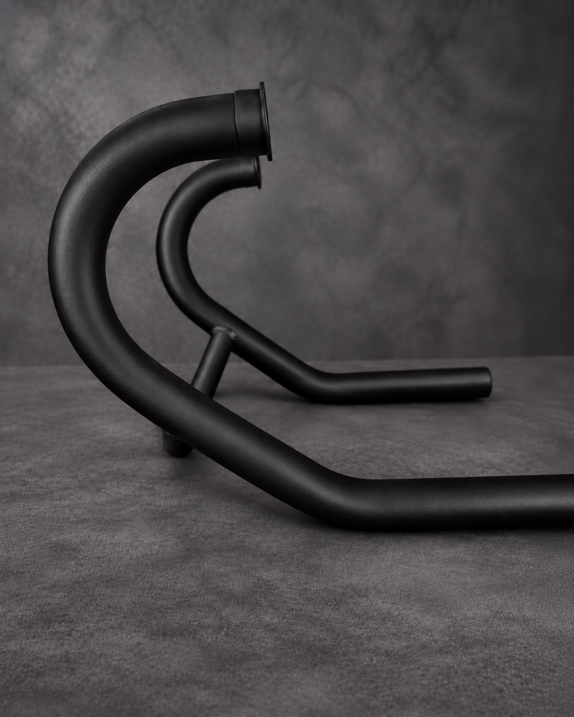 Black-coated curved motorcycle downpipes against a textured grey background