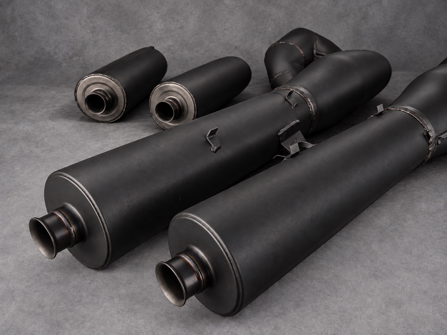 Black-coated exhaust expansion chambers and silencers arranged against a grey background