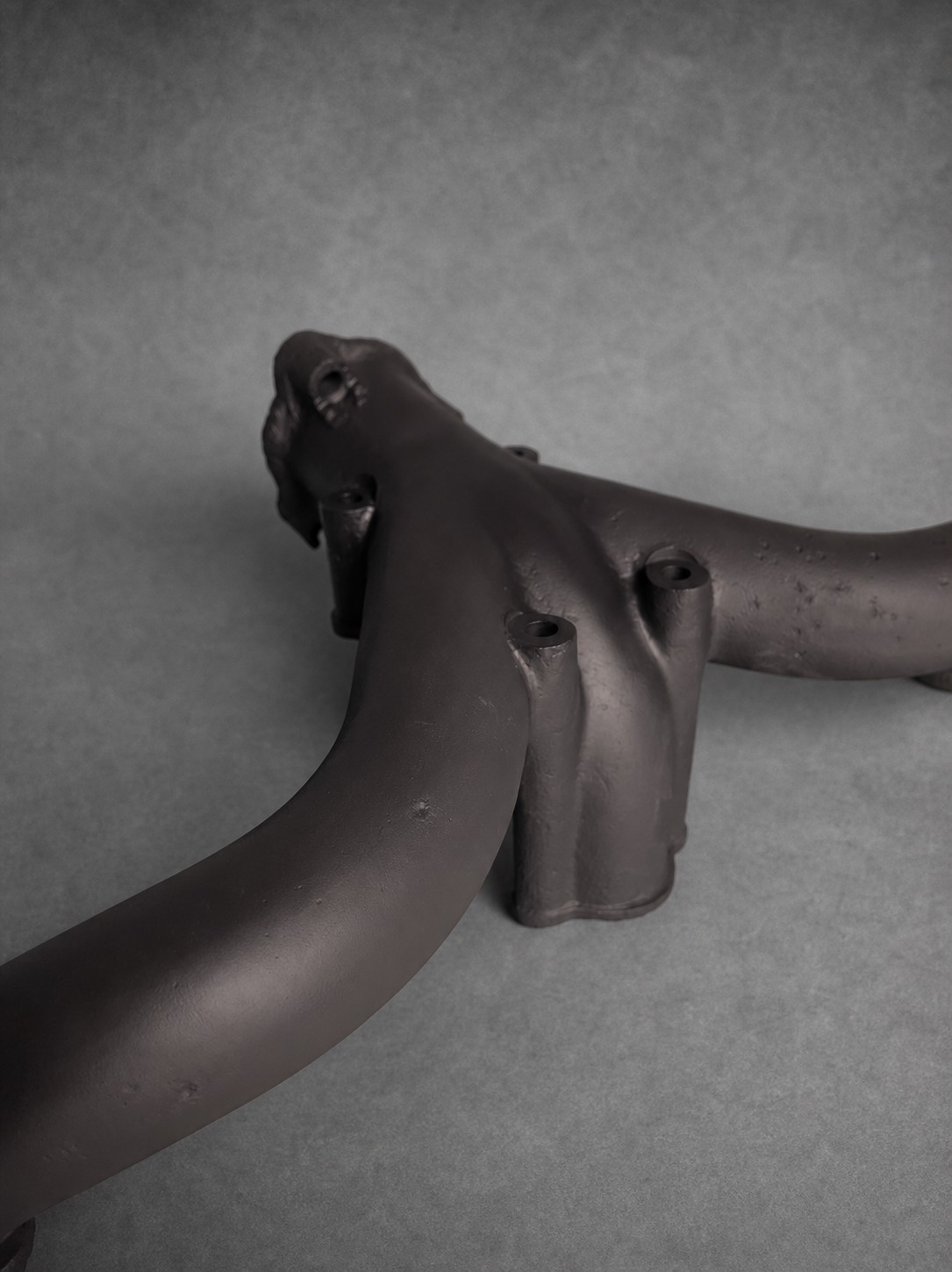 Detail of a dark-coated exhaust manifold with its casting texture preserved