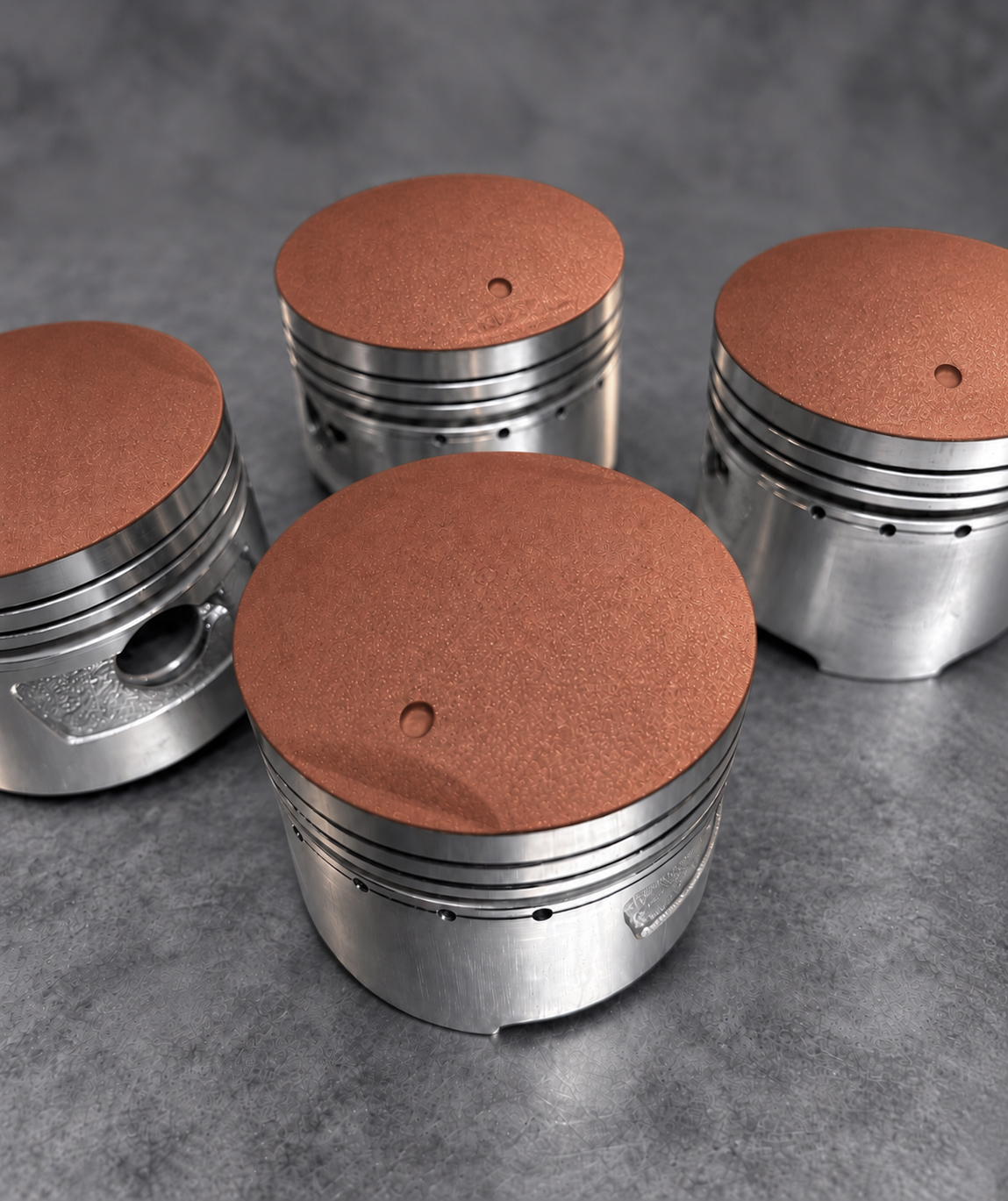 Four pistons with red ceramic-coated crowns and exposed alloy skirts and ring grooves