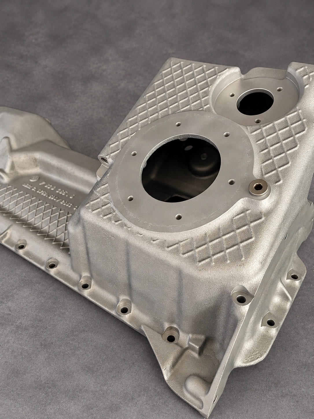 Close-up of a vapour-blasted alloy sump showing machined openings, threaded holes and cast reinforcement ribs