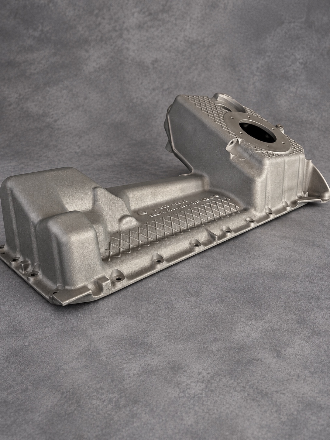 Side view of a vapour-blasted alloy sump showing cast texture, reinforcement ribs and its mounting flange
