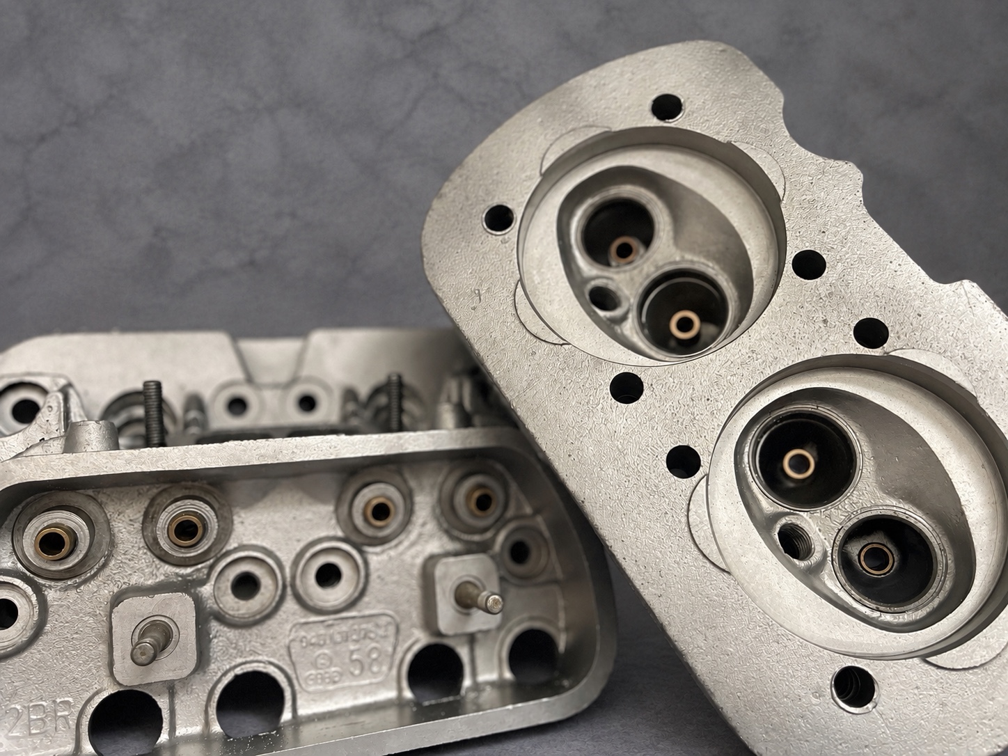 Two vapour-blasted cylinder heads showing upper faces and combustion chambers