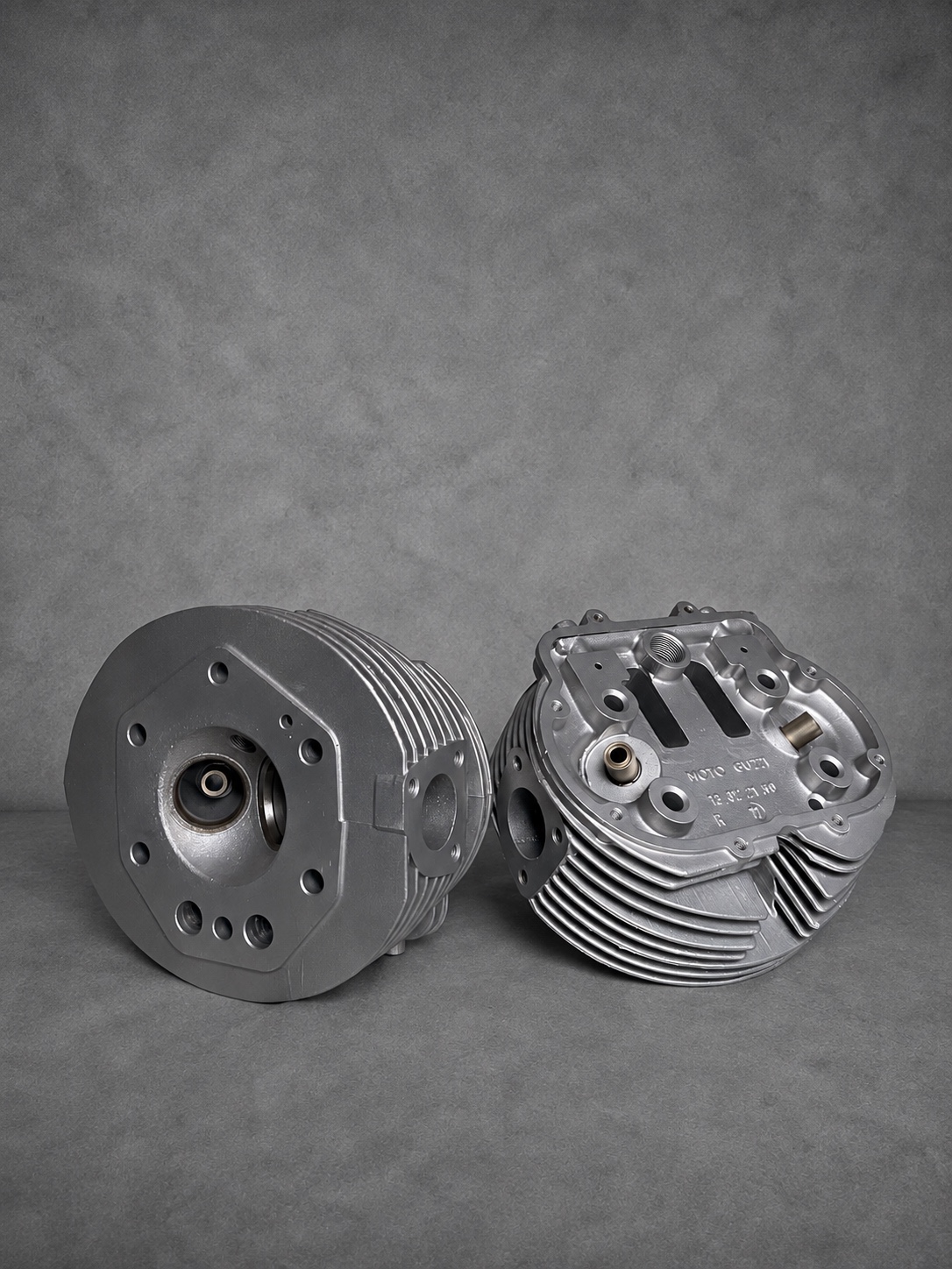 Pair of vapour-blasted Moto Guzzi cylinder heads showing combustion chamber and upper faces