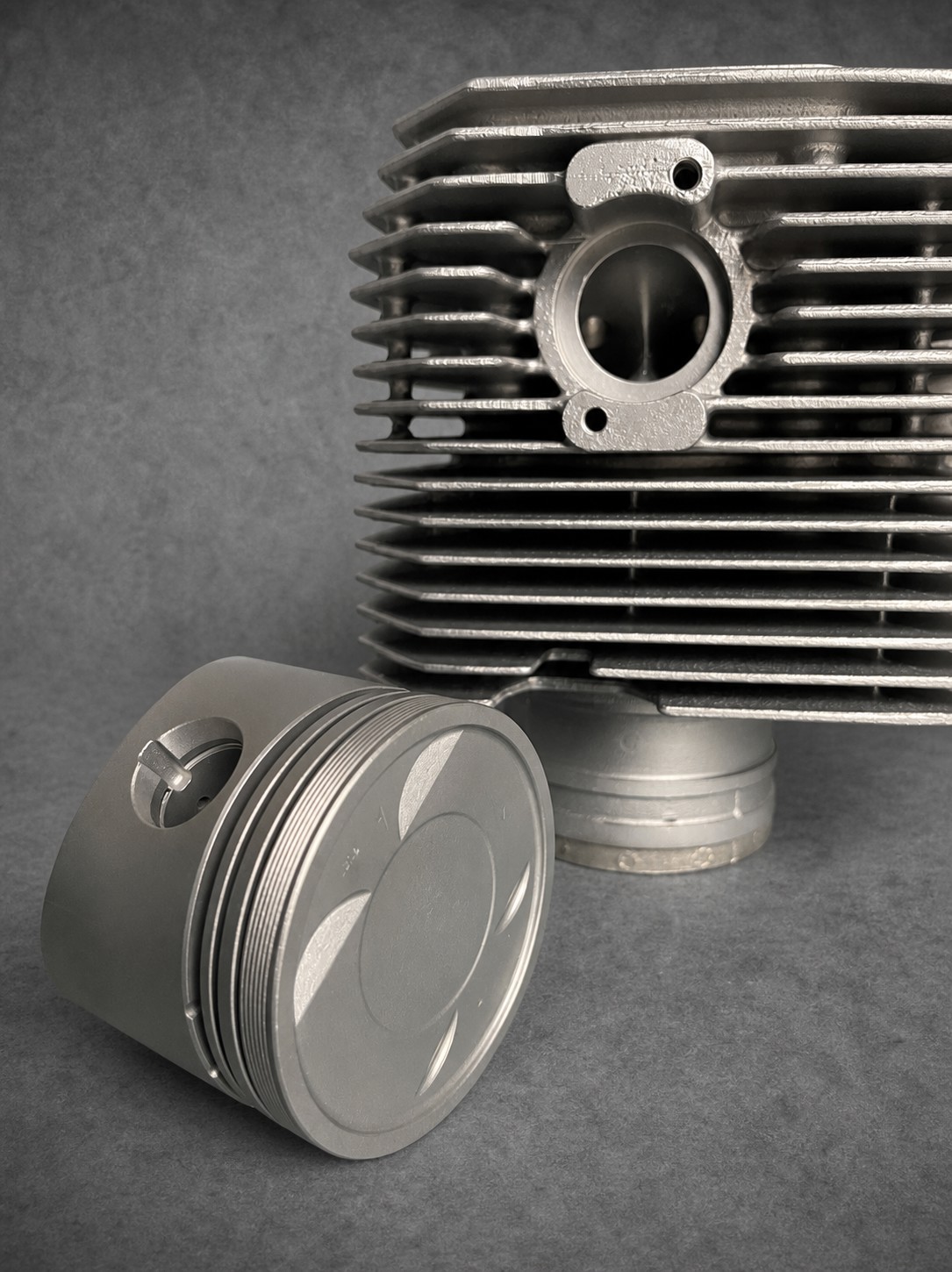 Close-up of a clean piston alongside vapour-blasted finned engine components